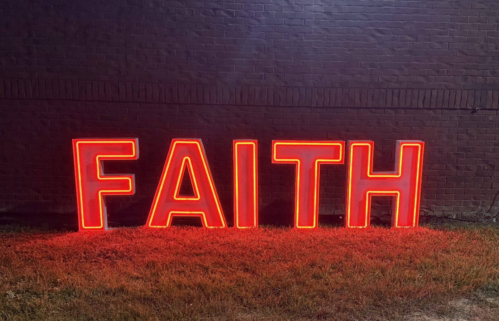 FAITH in red Illuminate letters against a brick wall at night