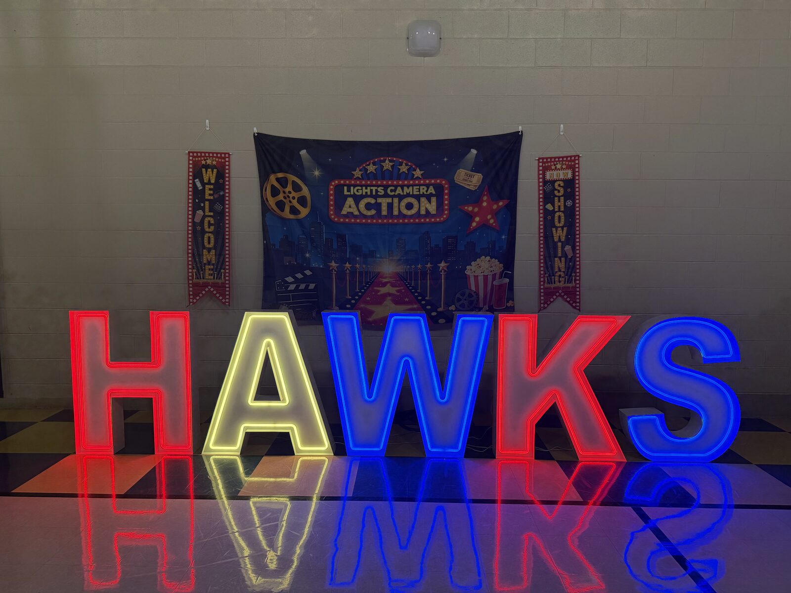 HAWKS in red, yellow, blue and green Illuminate letters in a school gym