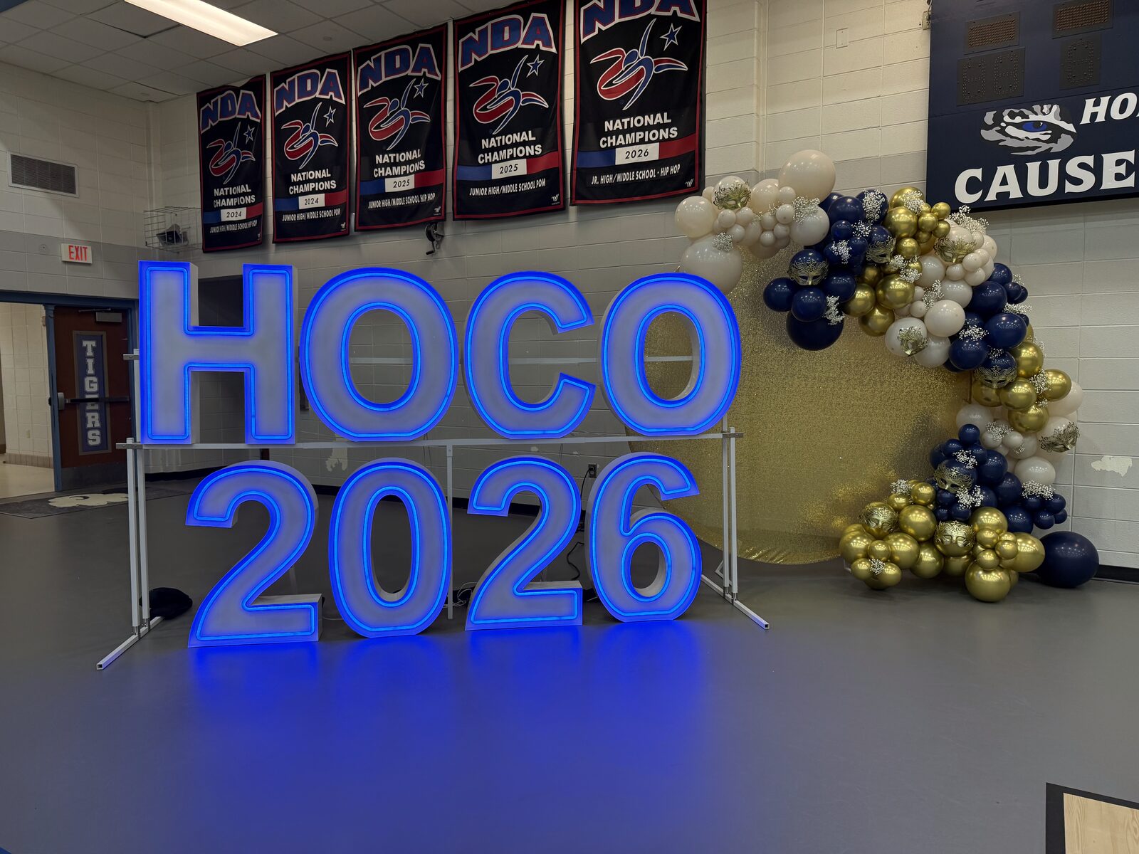 HOCO 2026 in blue Illuminate letters beside a navy and gold balloon garland