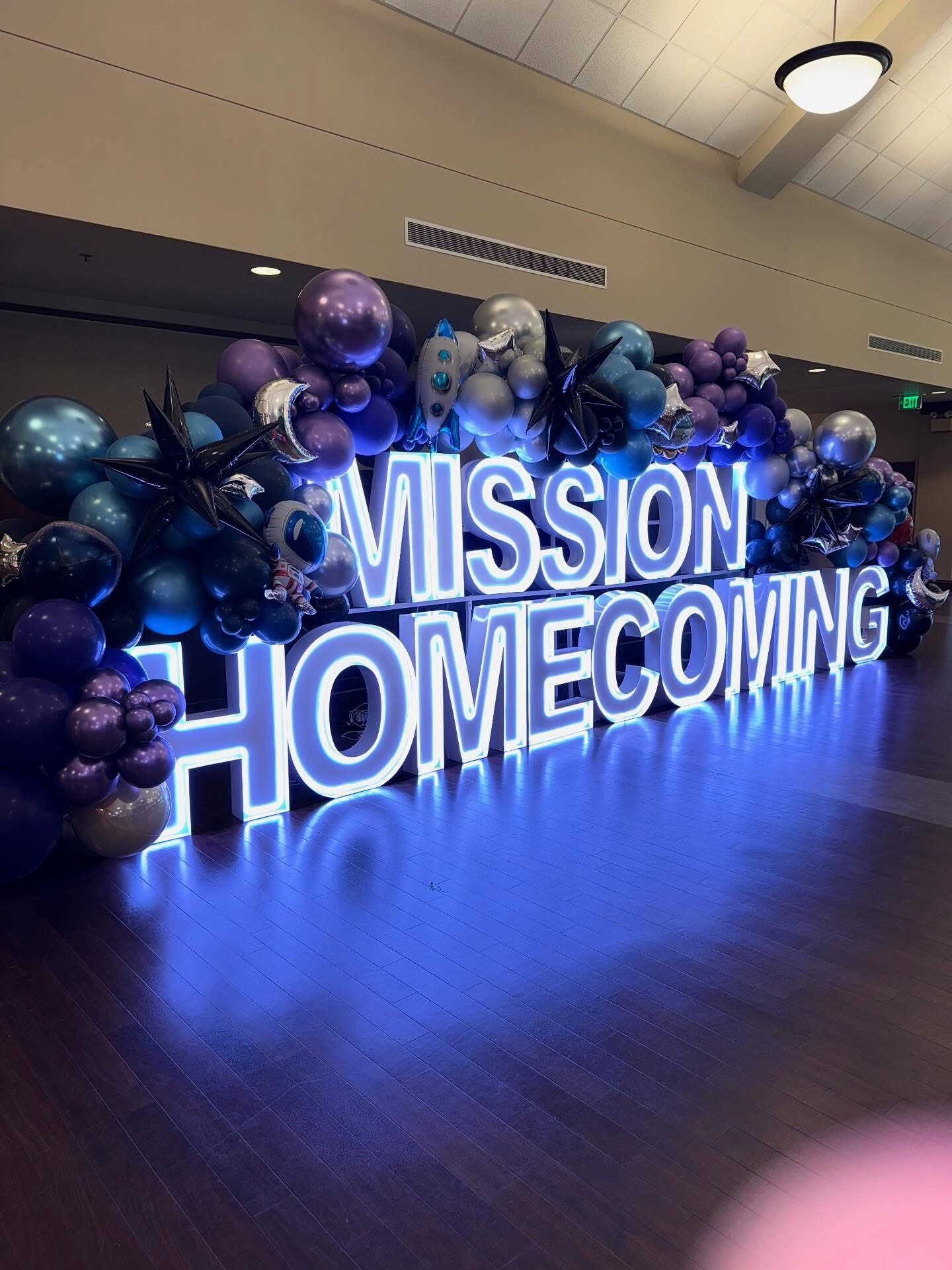 MISSION HOMECOMING in blue Illuminate letters under a balloon garland