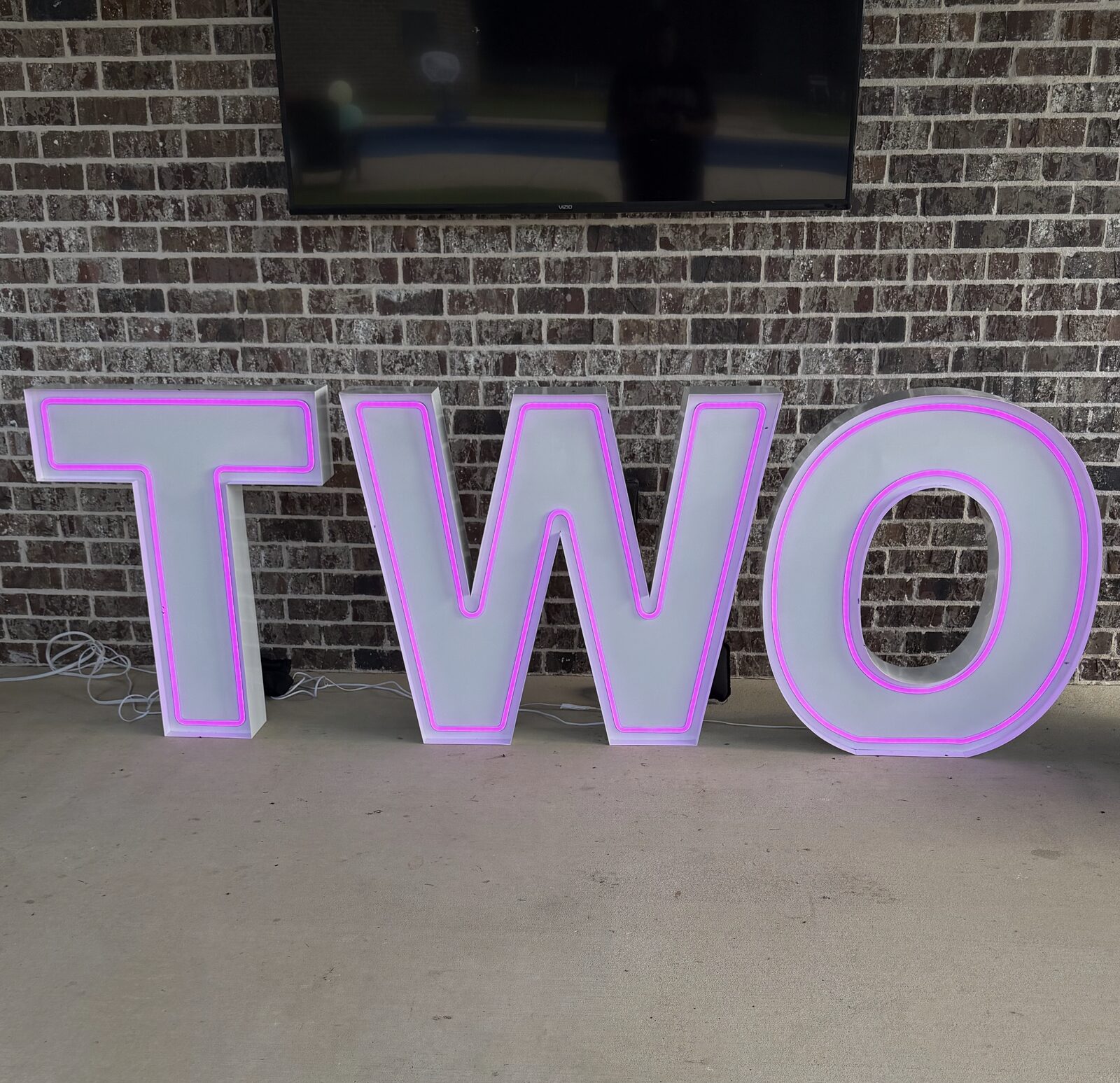 TWO in pink and purple Illuminate letters against a brick wall
