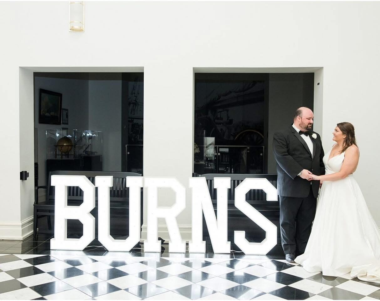 BURNS in lit letters on a checkered floor with a bride and groom