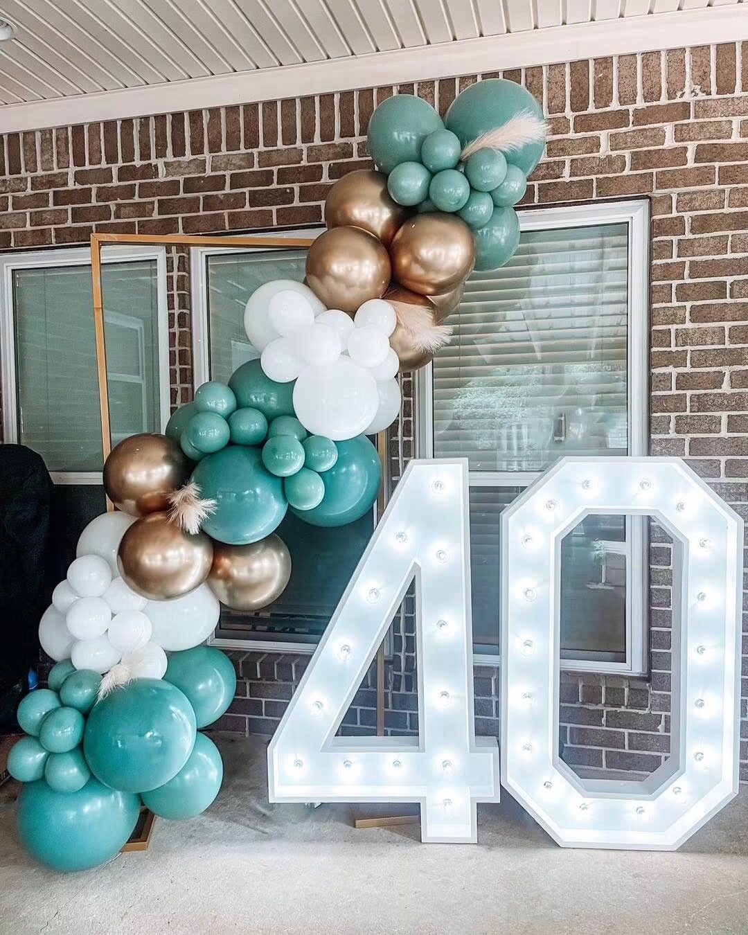 A lit 40 beside a teal, gold and white balloon garland
