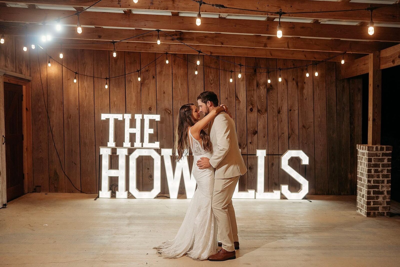 THE HOWELLS in lit letters in a barn reception with a bride and groom