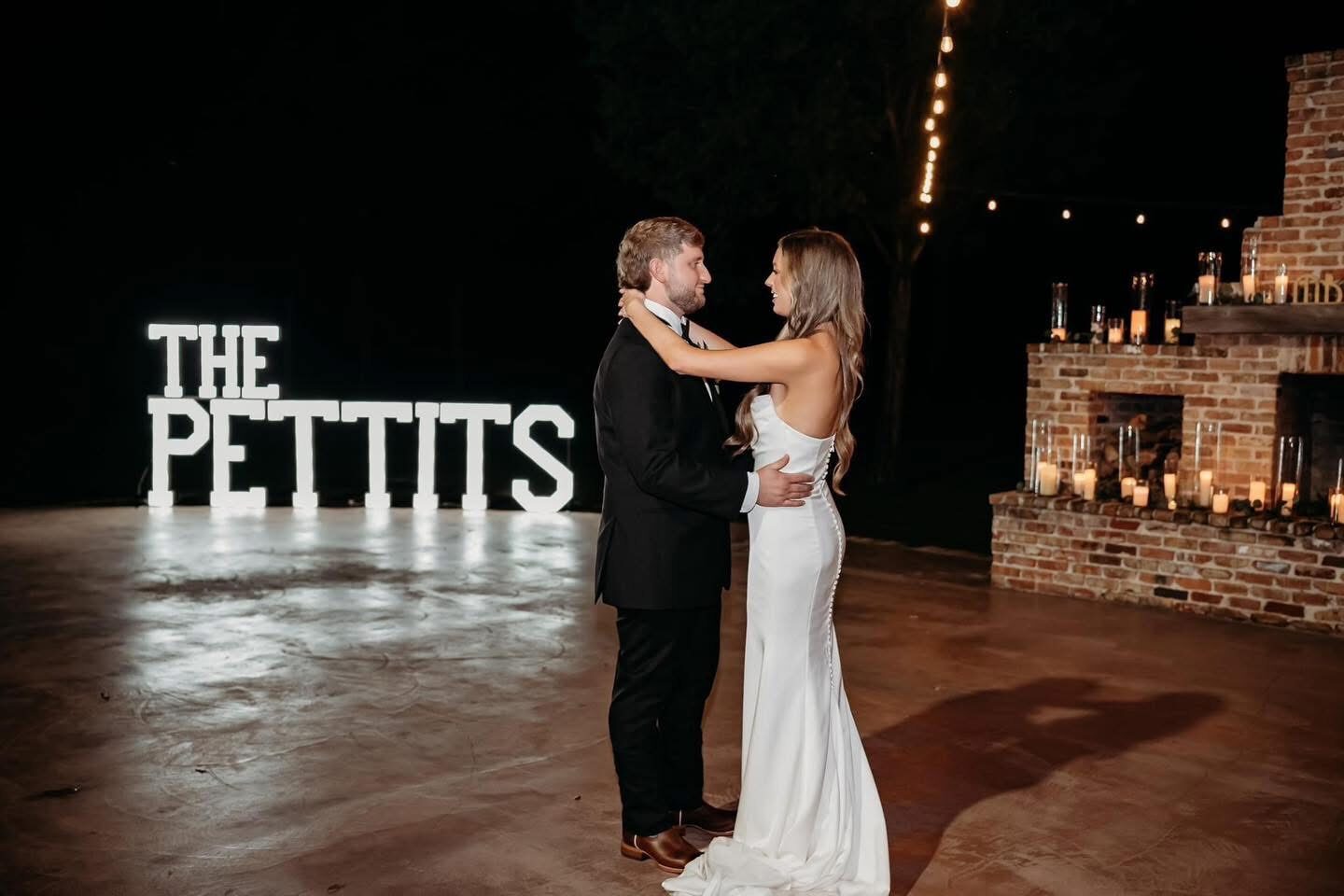 THE PETTITS in lit letters by an outdoor fireplace with a bride and groom