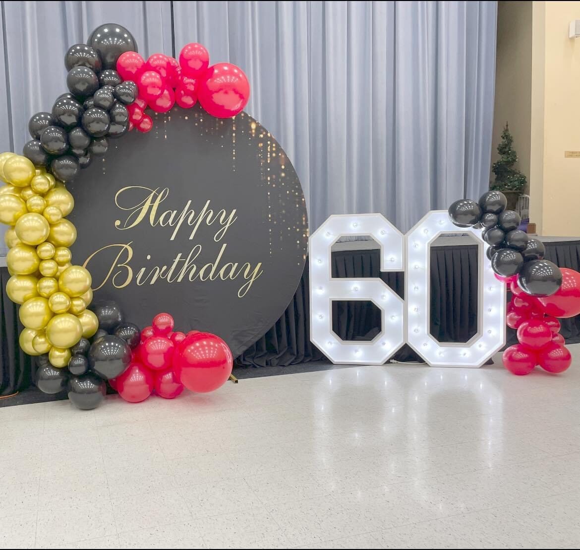 A lit 60 beside a Happy Birthday sign and a black and gold balloon garland