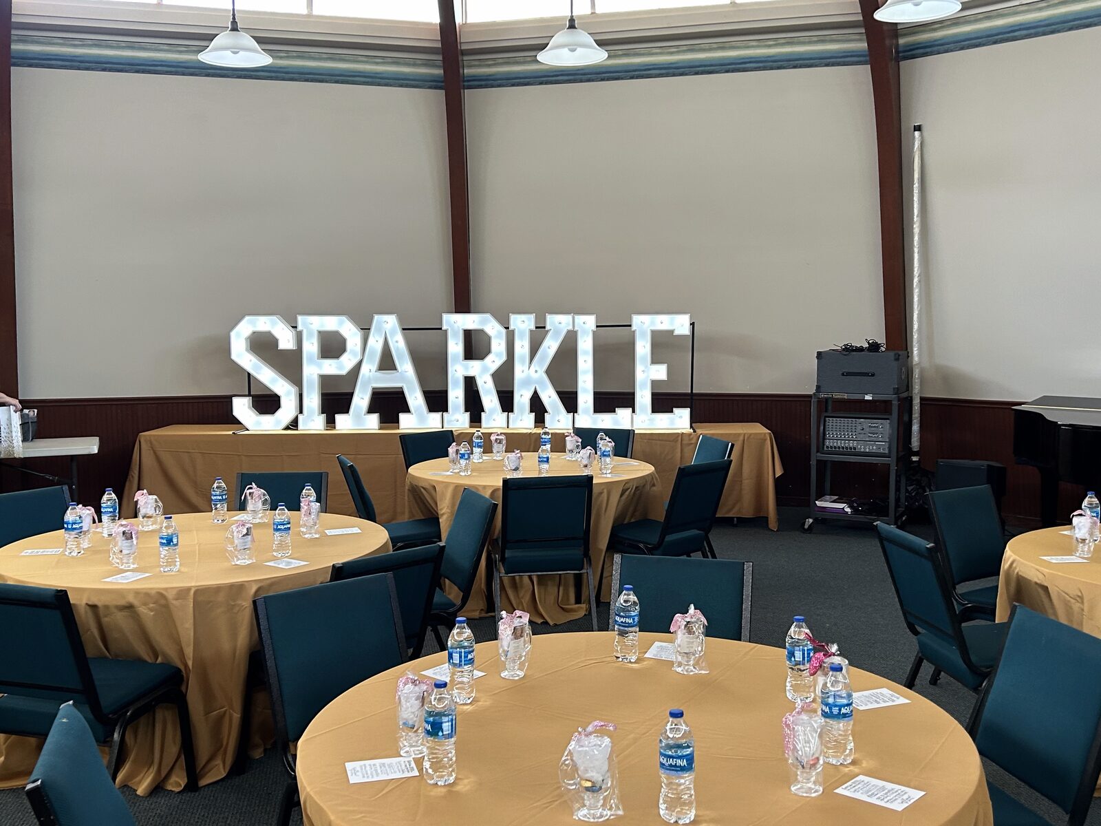 SPARKLE in lit letters behind banquet tables set for a meeting
