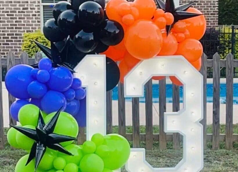 A lit 13 framed by orange, blue and green balloons beside a pool fence